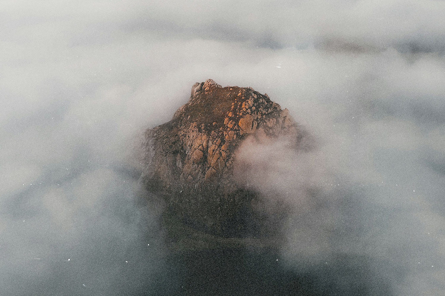 Rocky mountain peak emerging through thick, swirling clouds during golden light