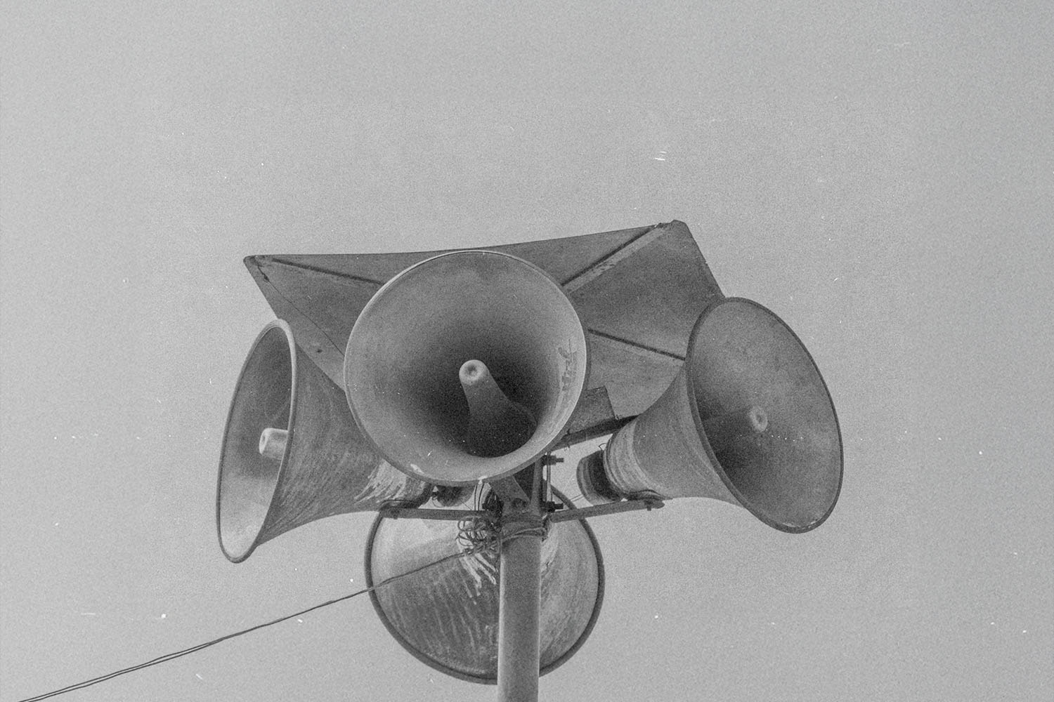 Cluster of large outdoor loudspeakers mounted on a tall metal pole against the sky