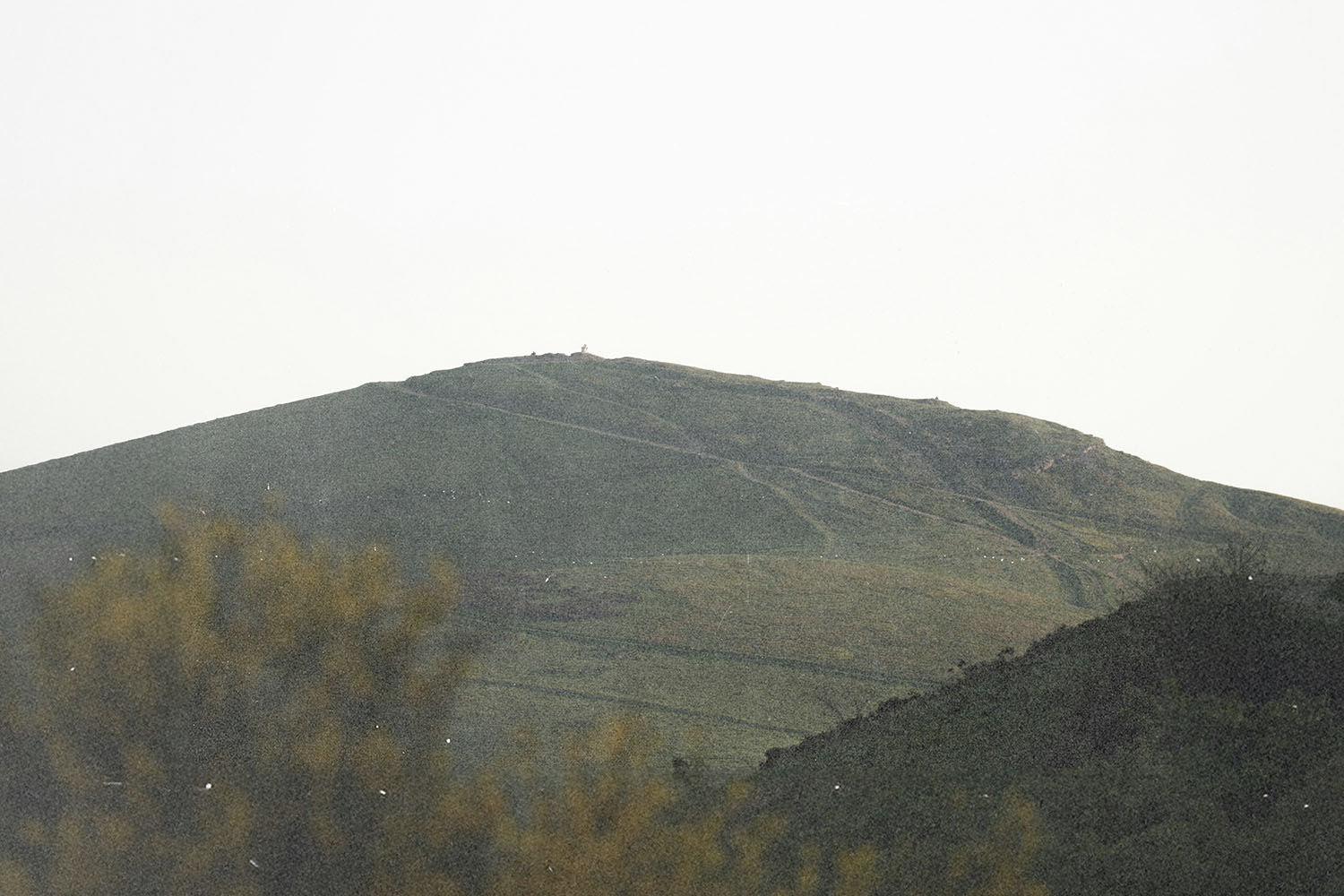 Green hillside with winding paths leading across the slope under a bright, hazy sky