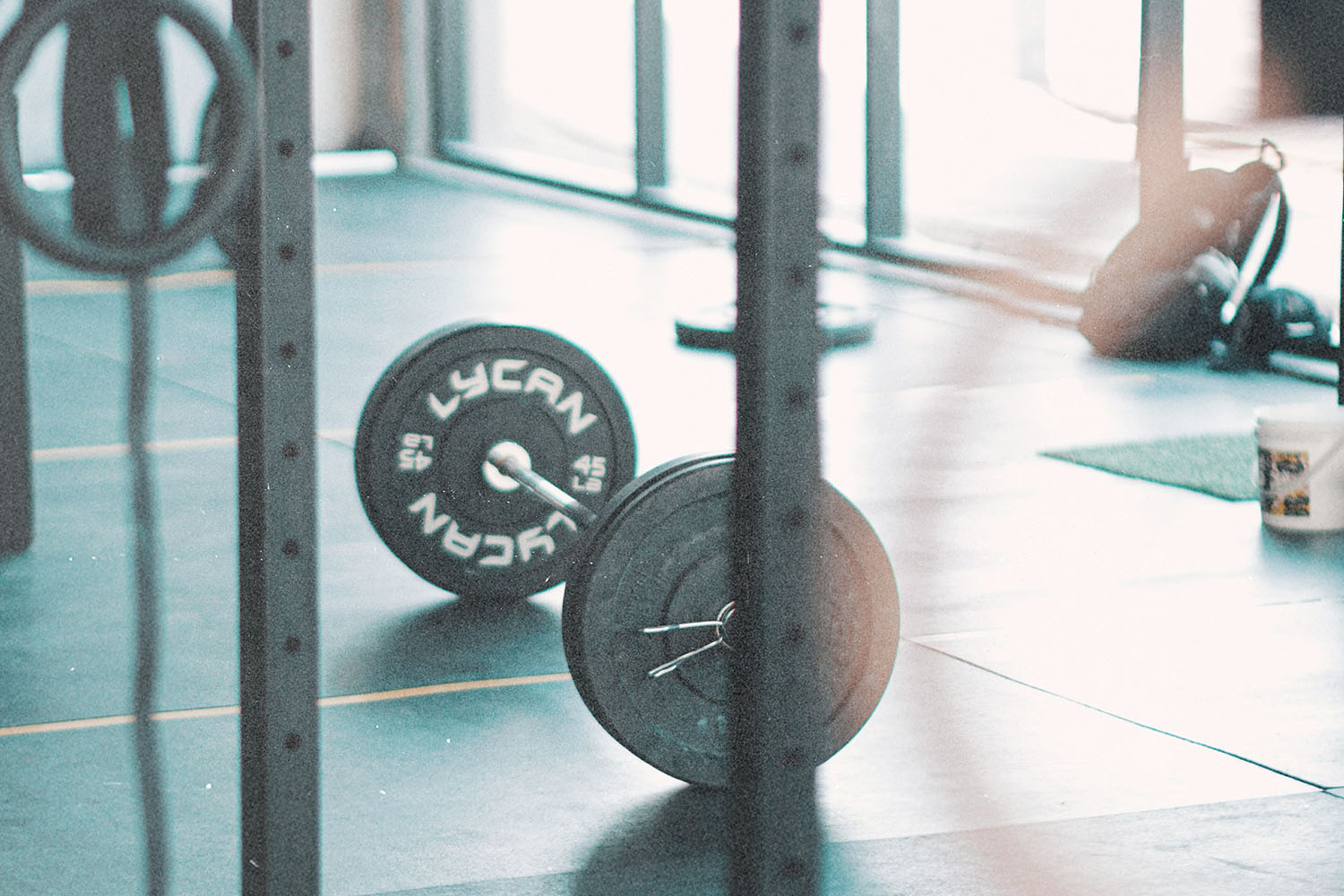 Loaded barbell resting on the floor of a gym near squat racks and natural window light