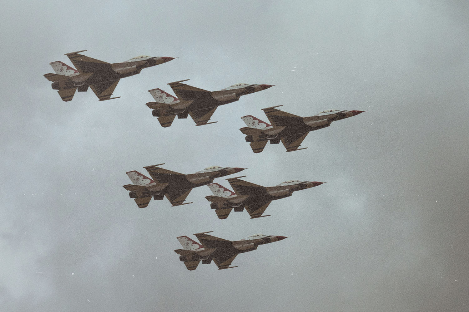 Formation of six military fighter jets flying together through a cloudy sky