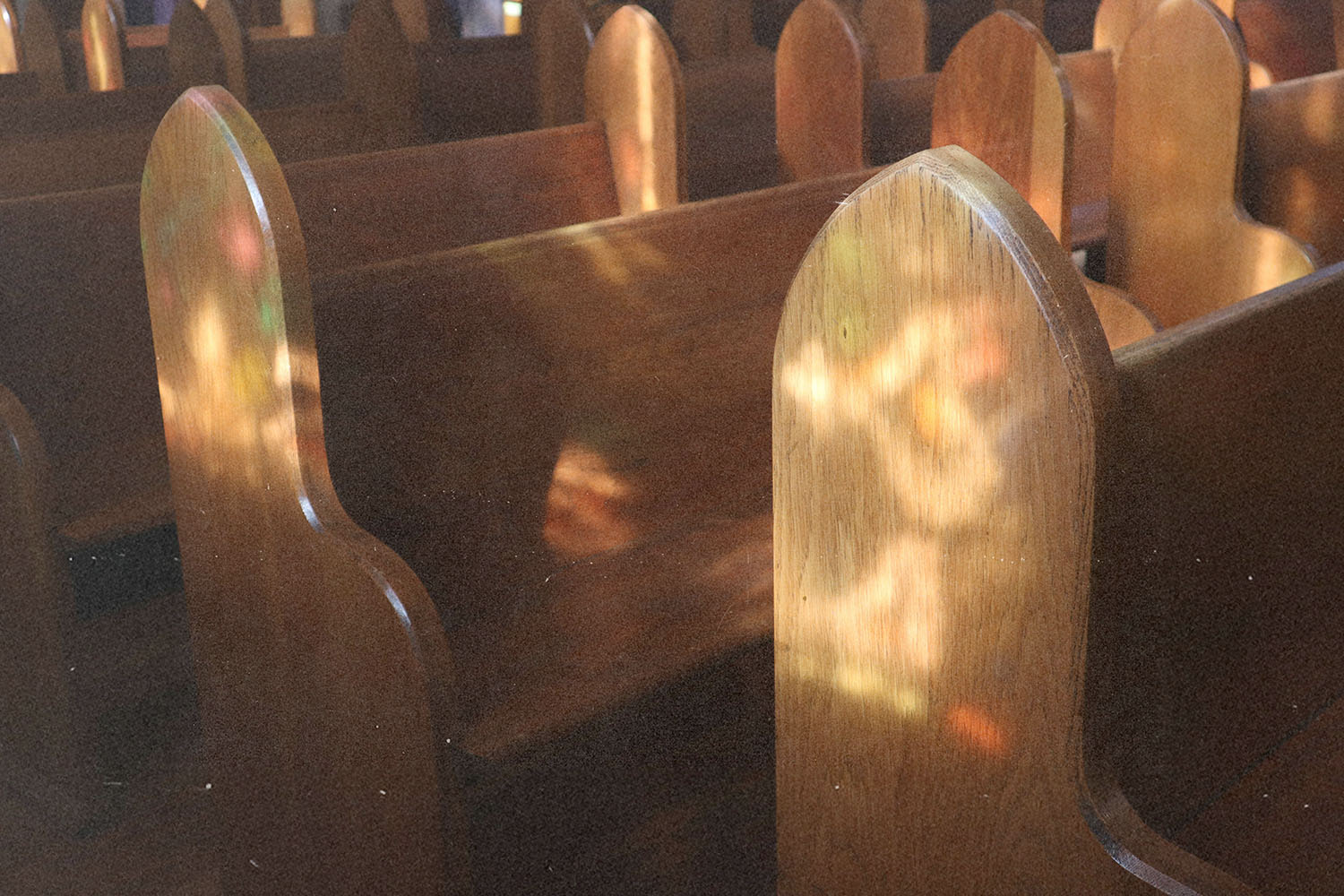 Empty wooden church pews illuminated by soft, colorful light filtering through stained glass