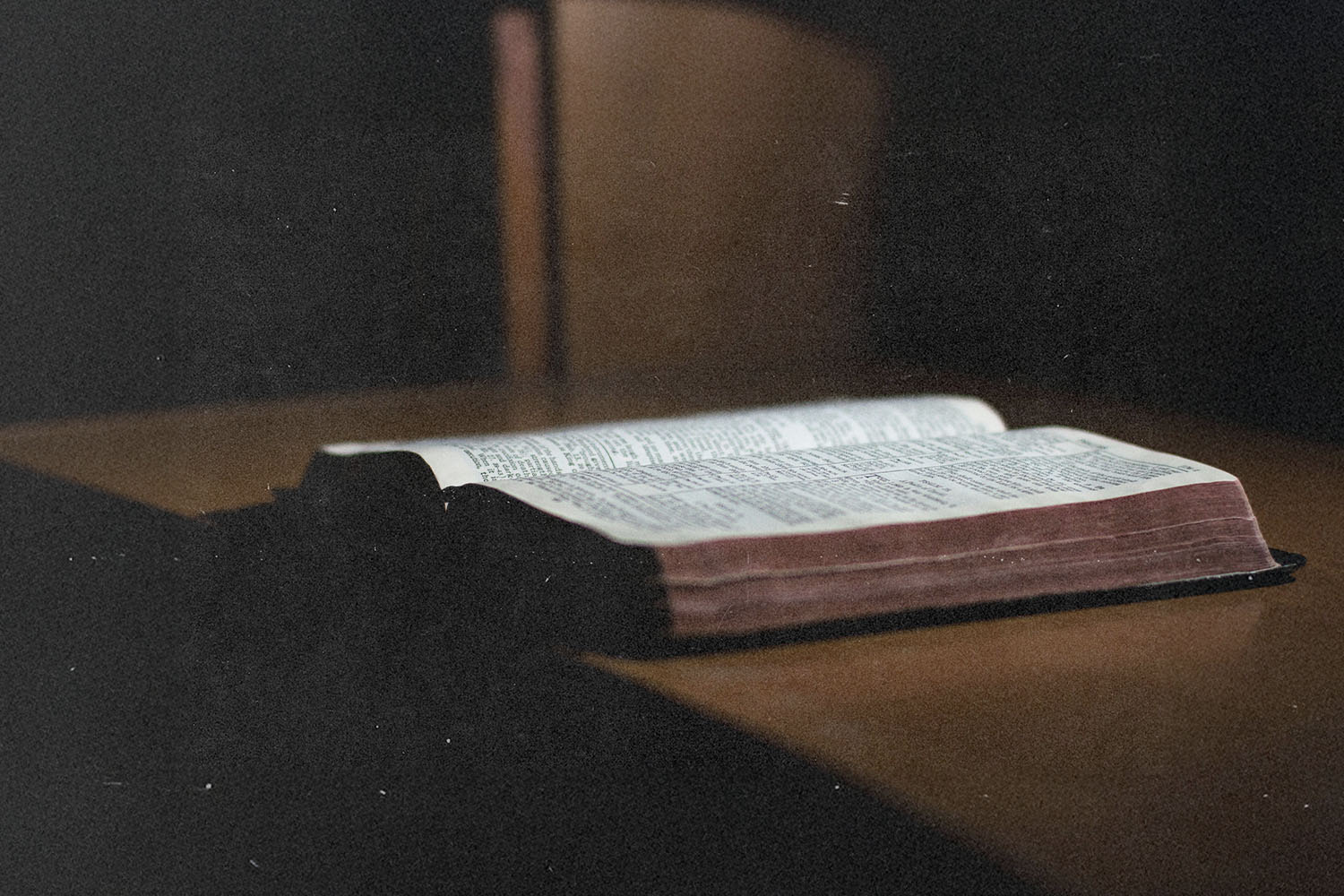 Open Bible resting on a wooden surface with soft light highlighting the printed text