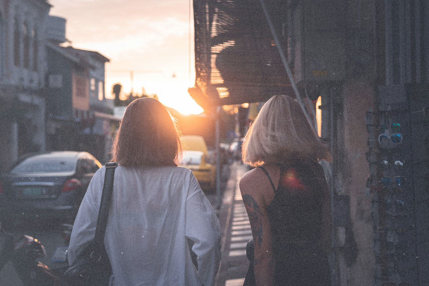 Two women walking down a city street at sunset with warm light shining between buildings