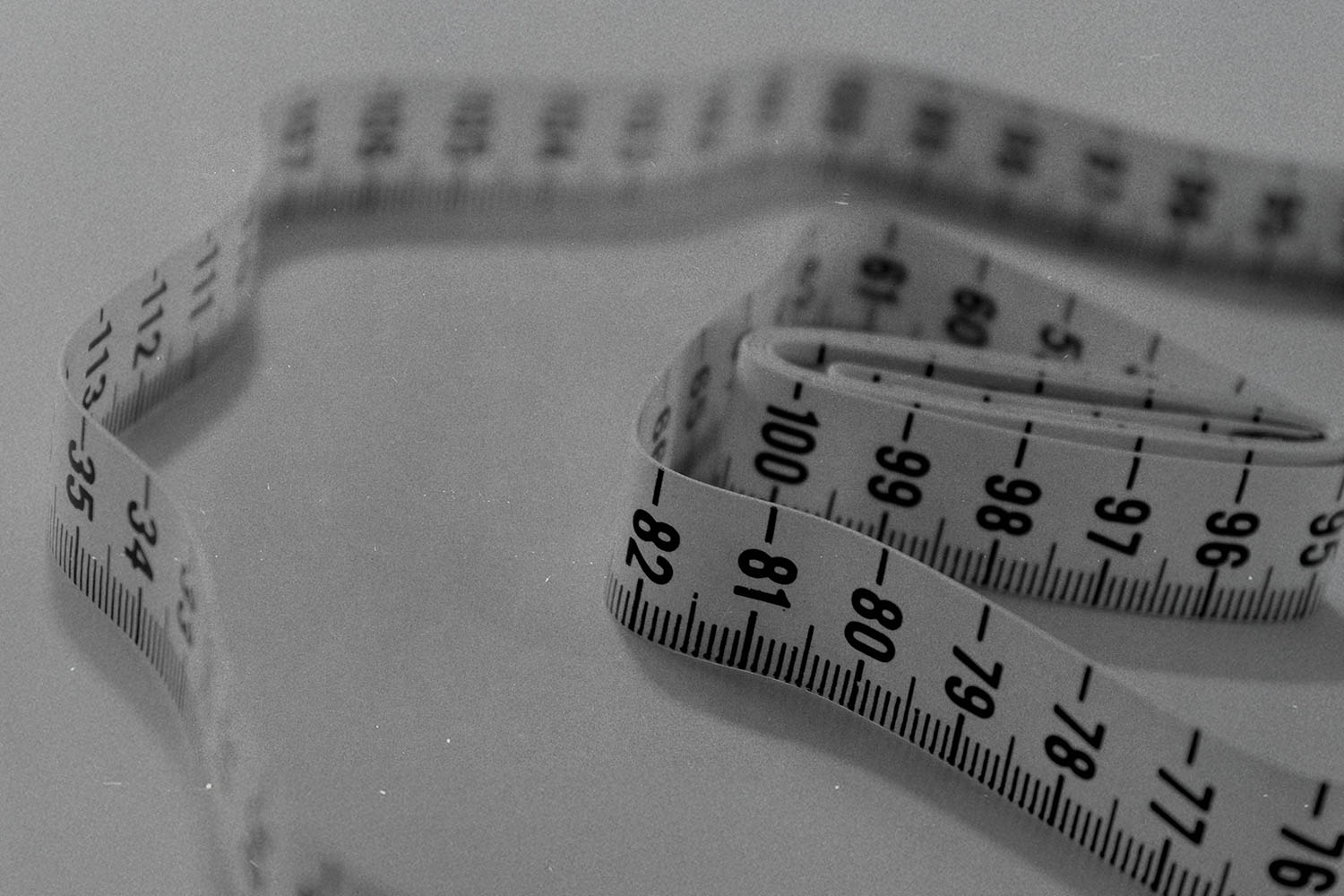 Flexible measuring tape coiled loosely on a flat surface in a black‑and‑white image