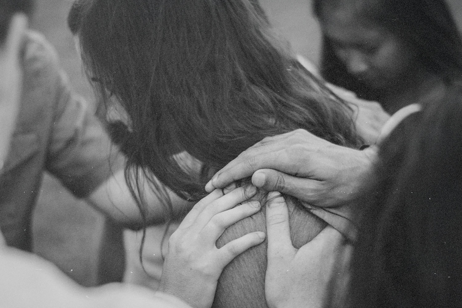 Several hands gently resting on a person’s shoulder in a supportive group setting