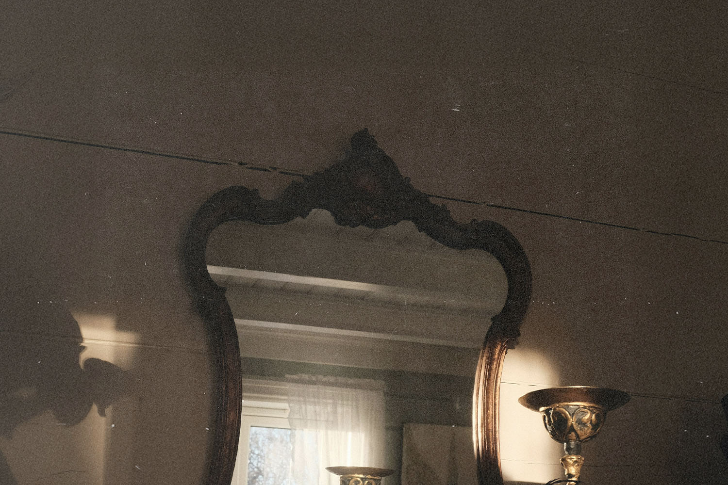 Ornate vintage mirror reflecting a softly lit room with a window and decorative lamp