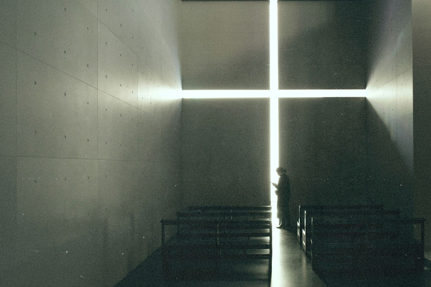 Silhouetted figure standing inside a dimly lit chapel before a large glowing cross-shaped window