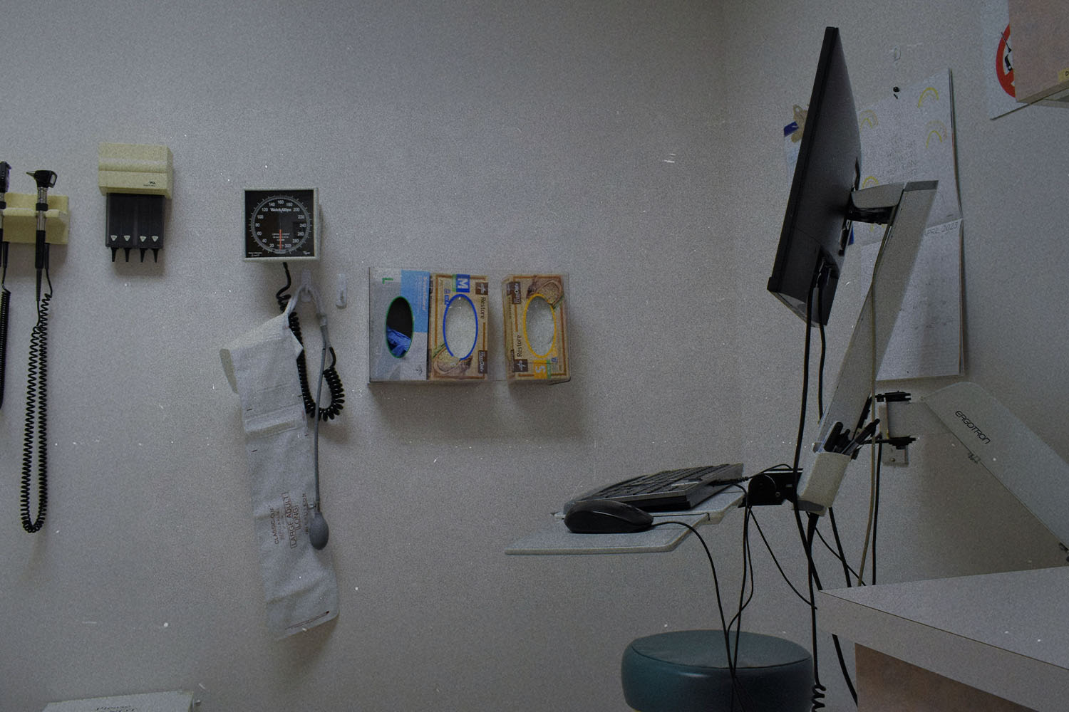 Medical exam room with wall-mounted diagnostic tools, glove boxes, and a computer workstation