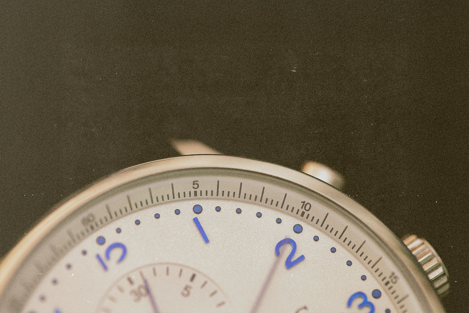 Close-up view of an analog watch face showing the numbers one through three and fine minute markings, with a metal casing partially visible against a dark background