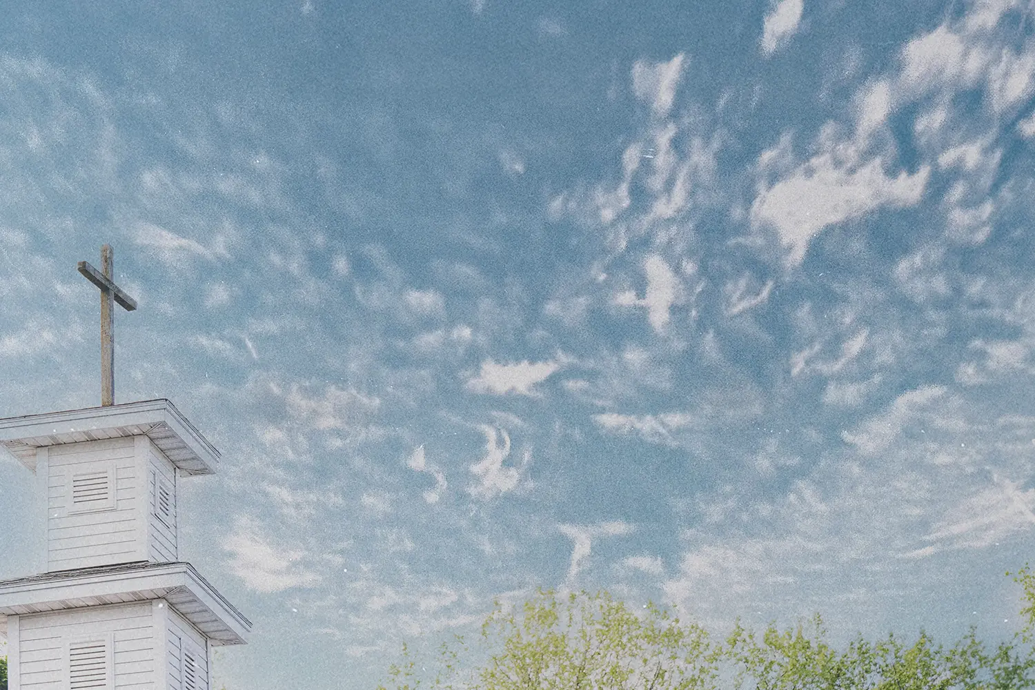 White church steeple with a cross on top set against a bright blue sky with scattered clouds