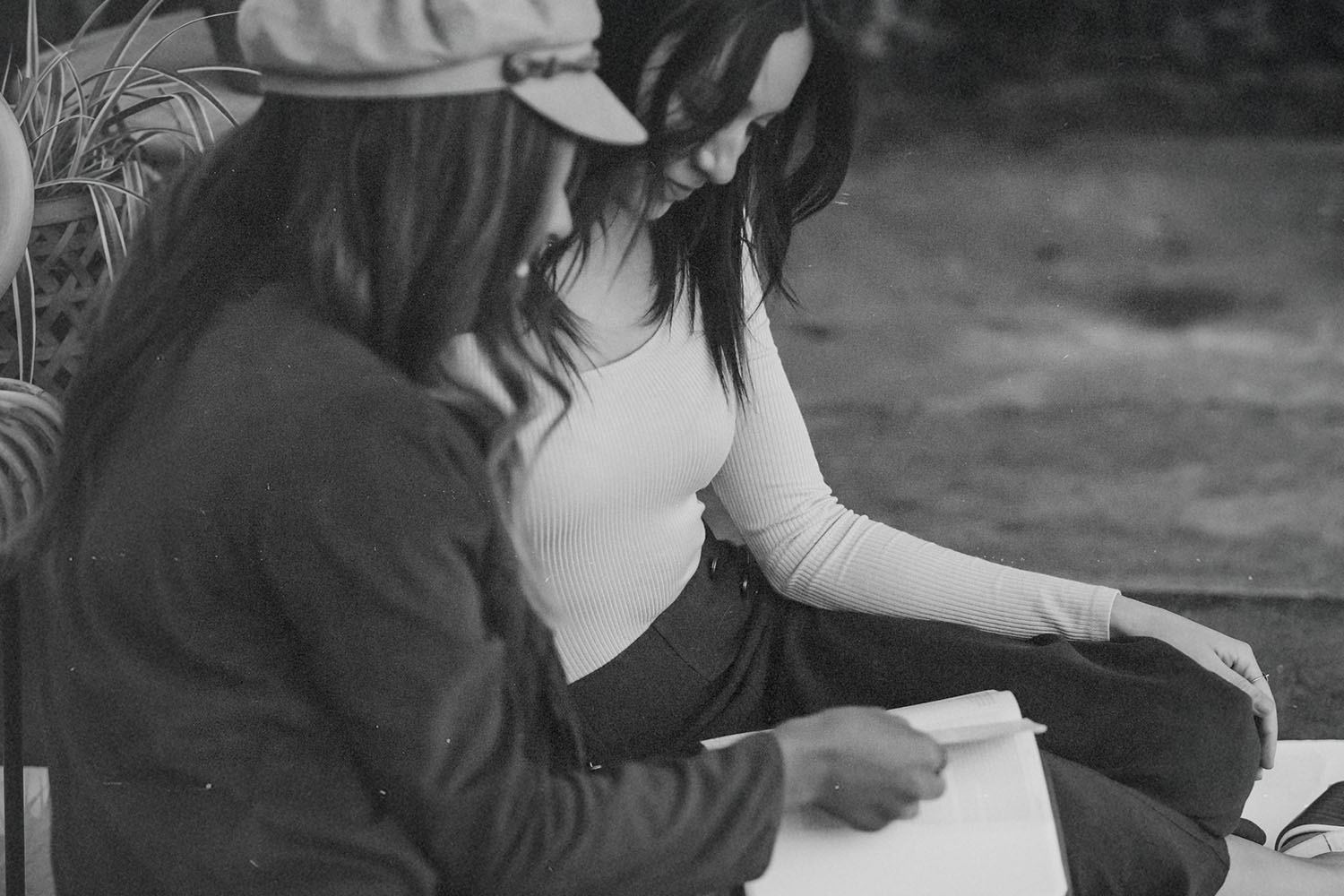 Two people sitting together outdoors, reading and discussing an open book in a relaxed setting