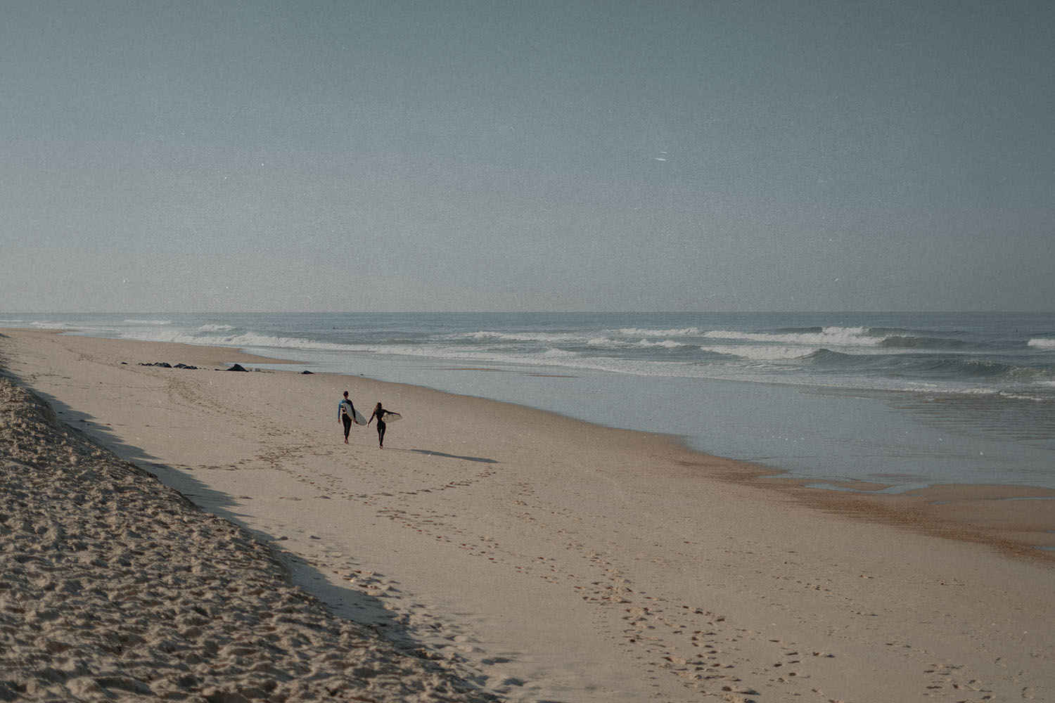 Couple walking along an empty sandy beach beside gentle ocean waves
