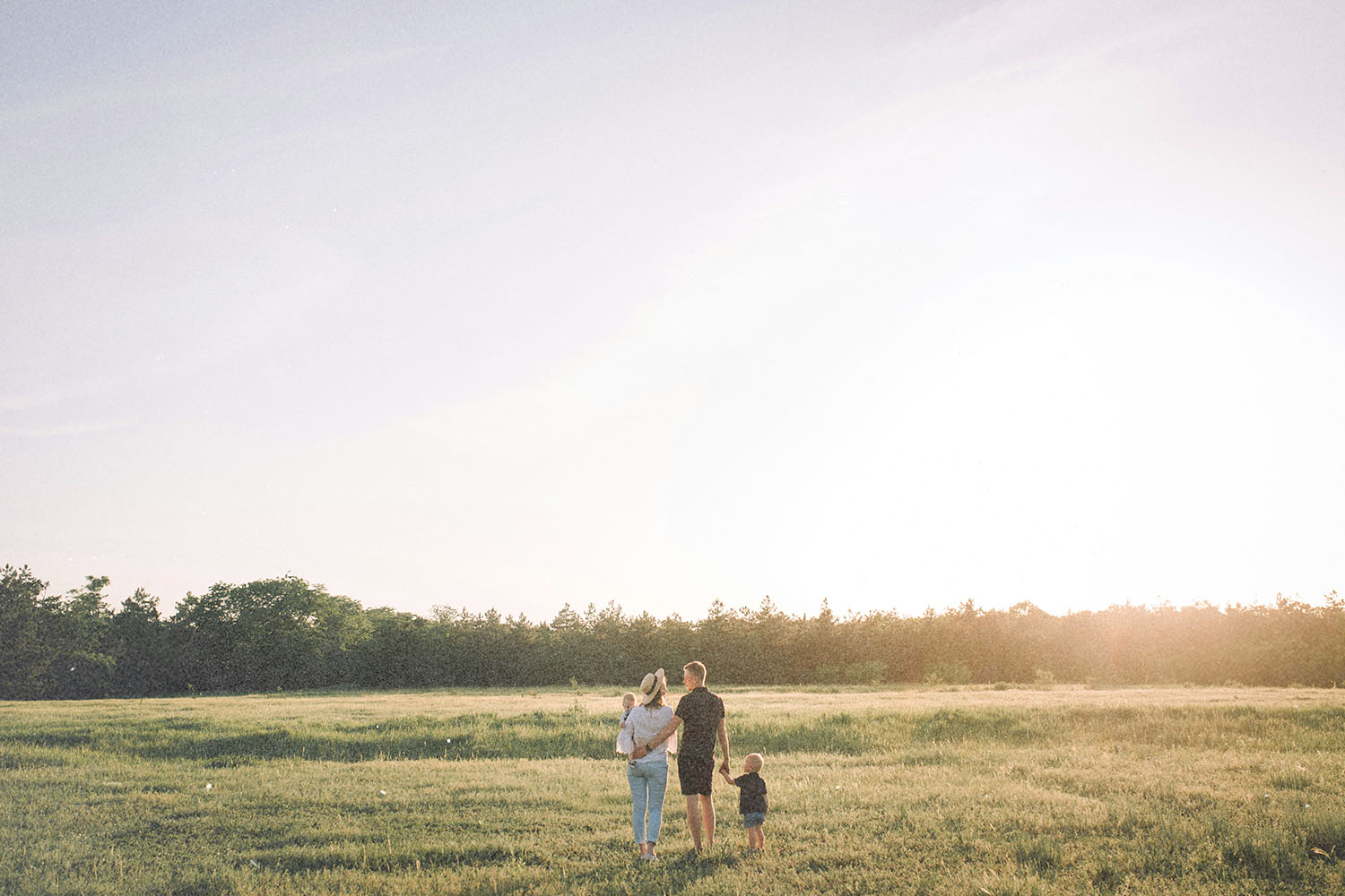 A family walking together through an open grassy field at sunset, holding hands and enjoying the warm light