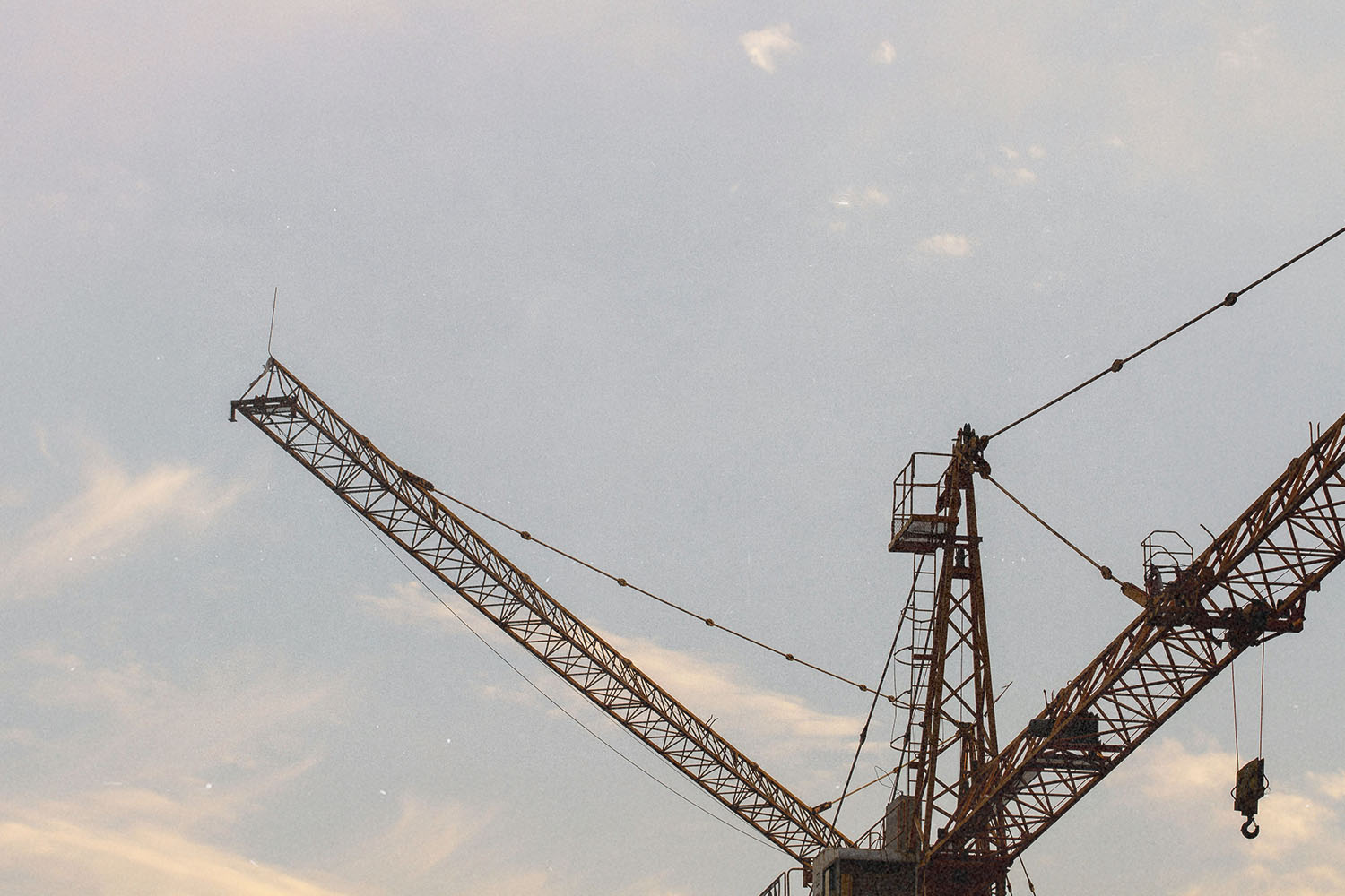 Construction cranes silhouetted against a soft evening sky with light clouds