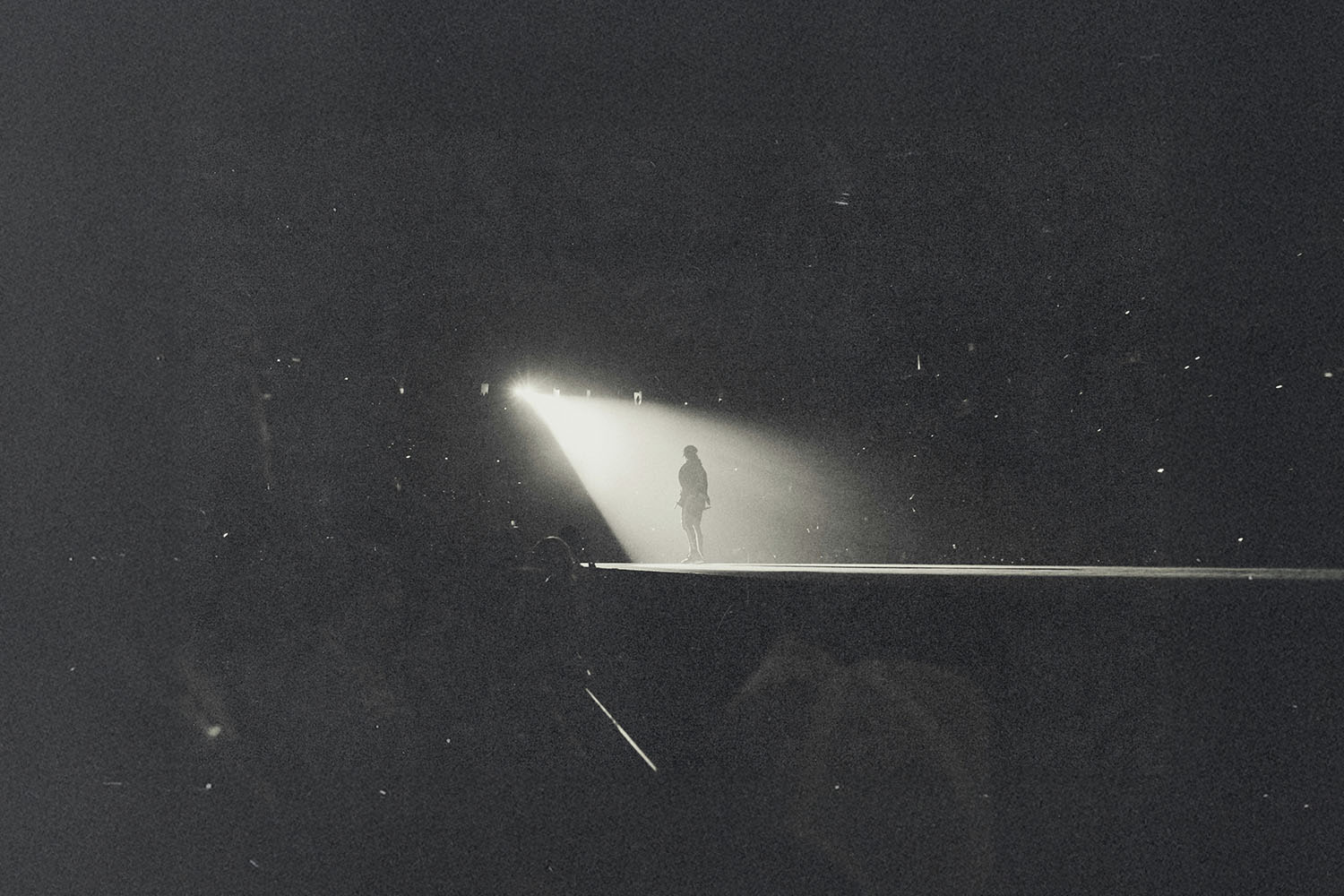 Silhouetted figure standing alone in a bright spotlight on a dark stage