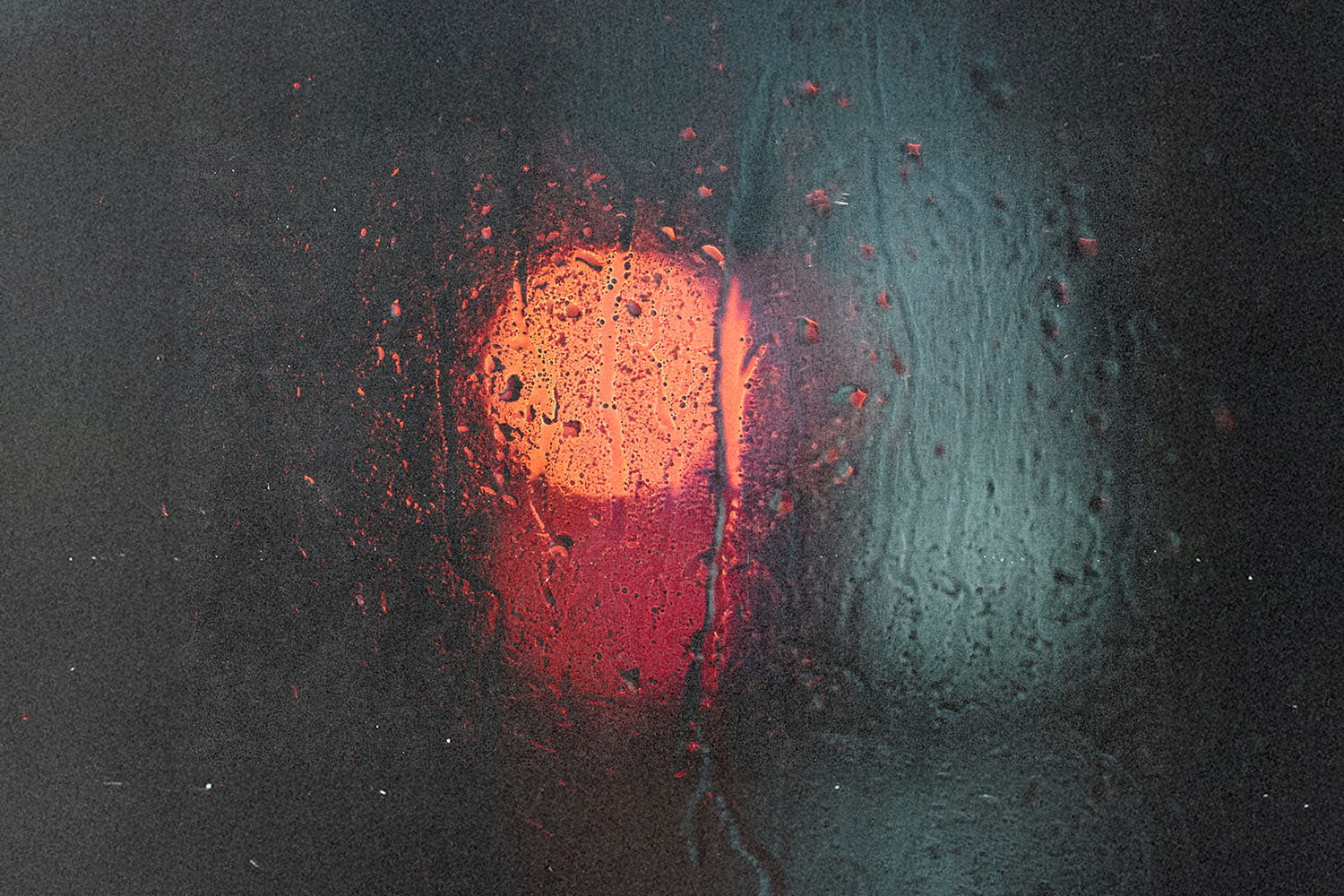 Blurred red and blue lights shining through a rain‑covered window