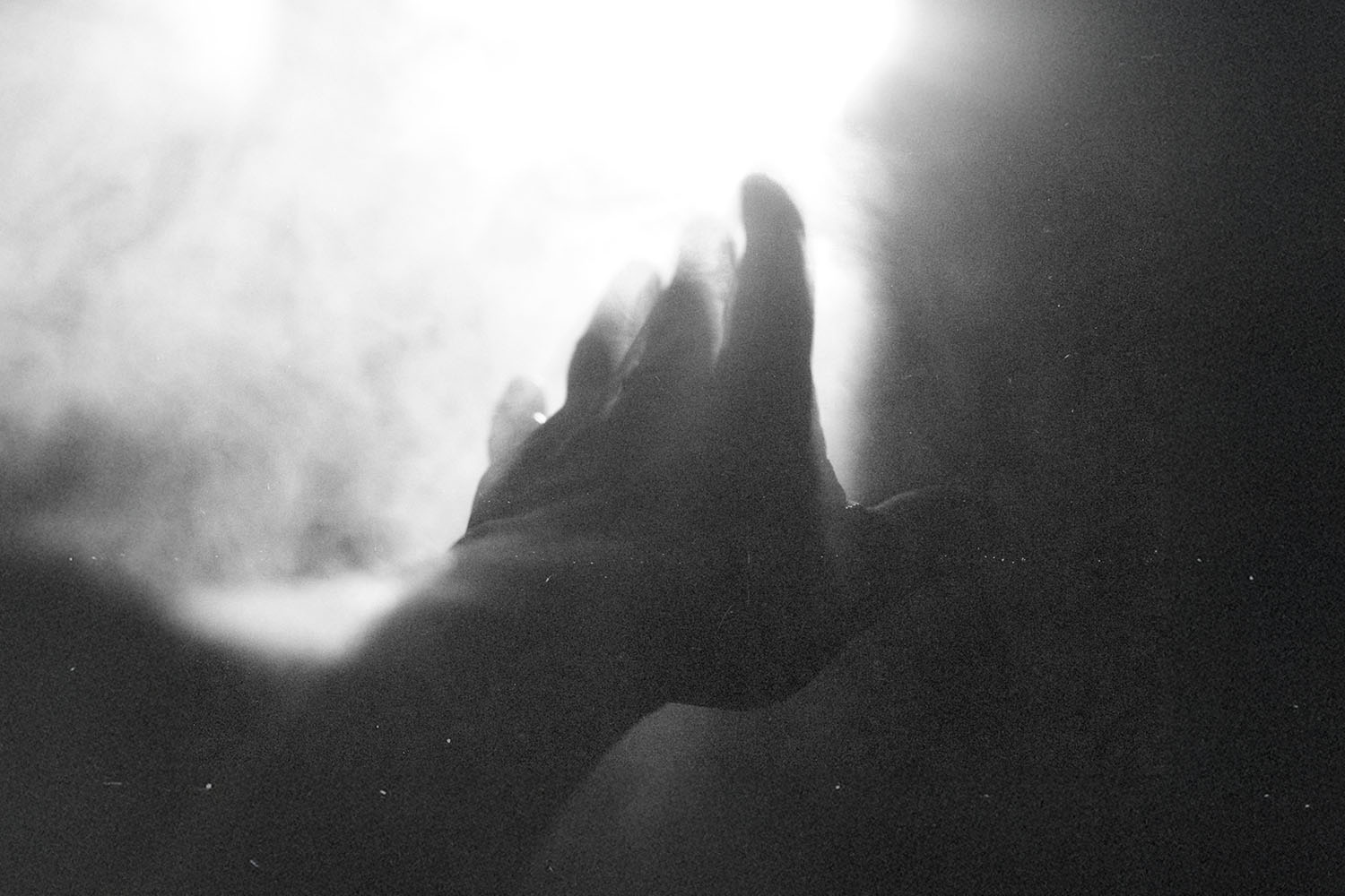 Hand reaching toward a bright light surrounded by soft, glowing mist in a black‑and‑white scene