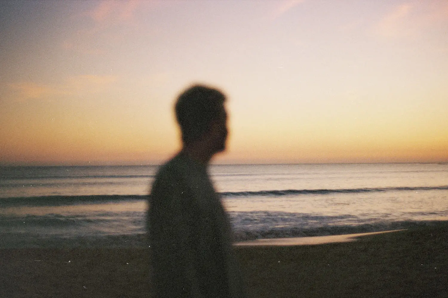 Silhouetted figure standing on the beach at sunset with gentle waves rolling onto the shore