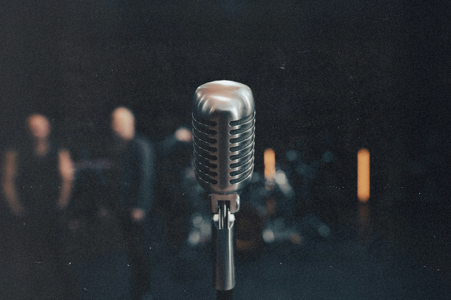 Vintage-style microphone in sharp focus on a dimly lit stage with blurred figures and lights in the background
