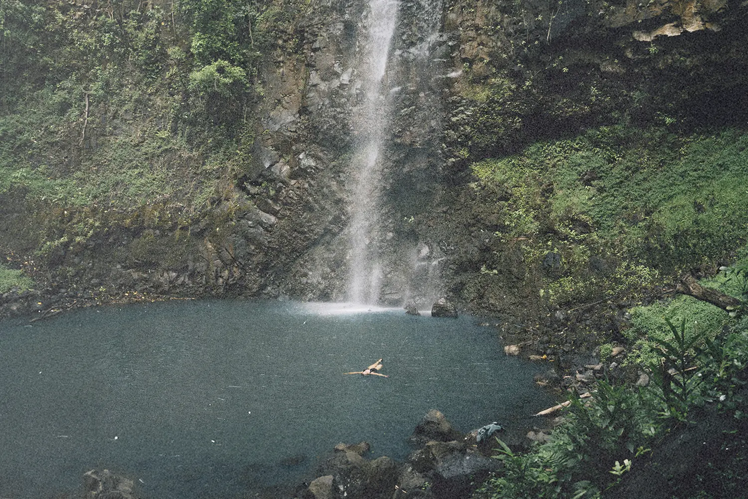 Waterfall flowing into a blue pool with a person swimming below