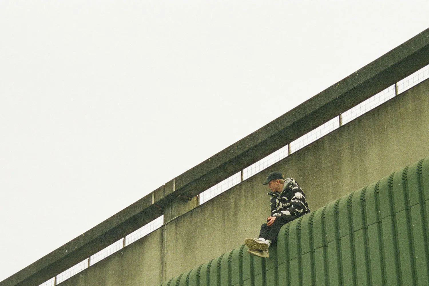 Silhouetted figure standing at the top of a walkway lined with tall flagpoles under a hazy evening sky