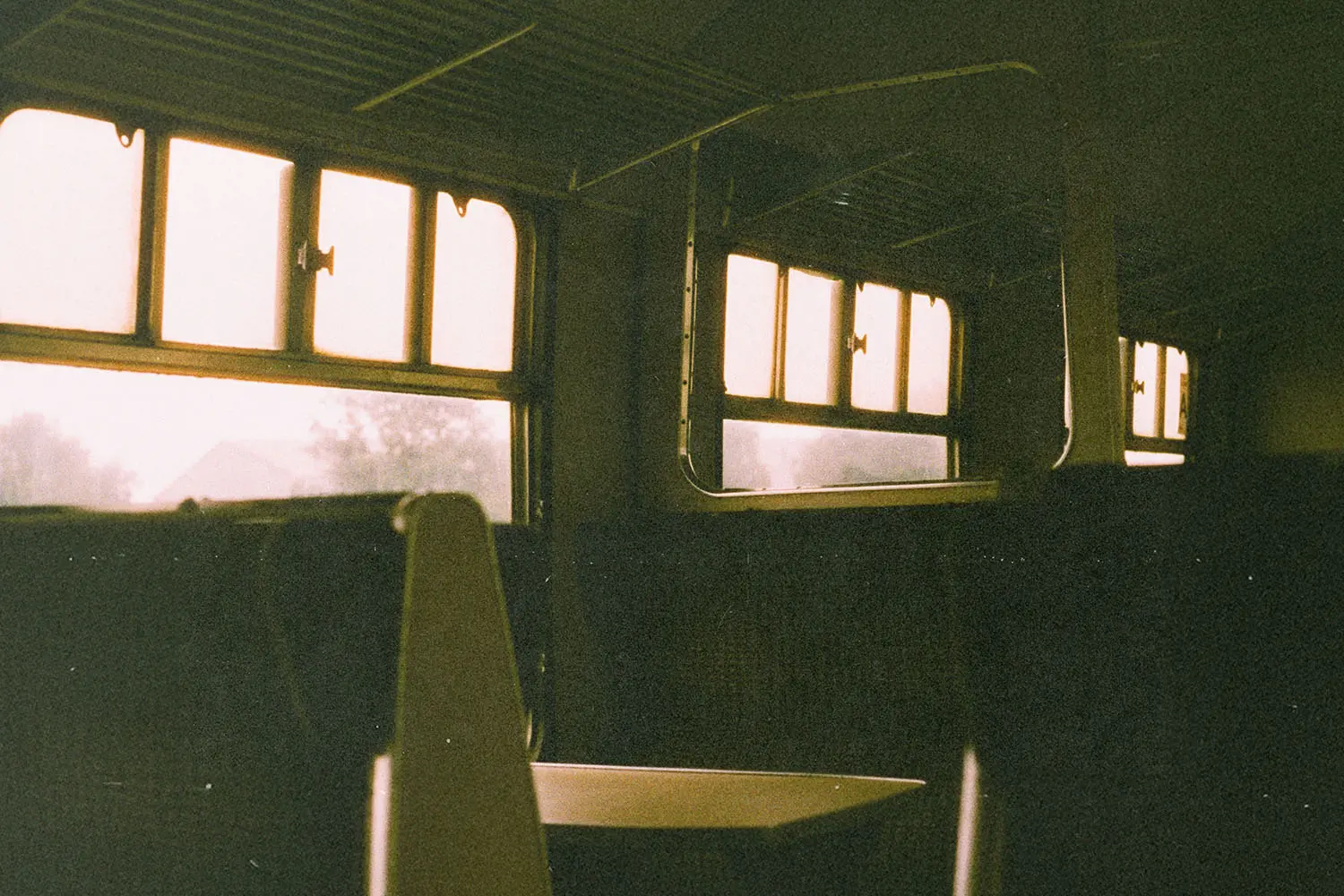 Empty train seats and sunlit windows inside an old-fashioned railway carriage, with warm light filtering through the glass