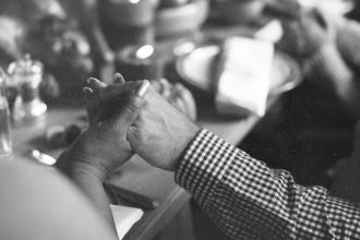 Two people hold hands across a table set with plates, bowls, and candles in a warm, intimate setting