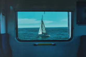 Sailboat on a calm blue ocean framed perfectly within a train window, with clear sky above the horizon