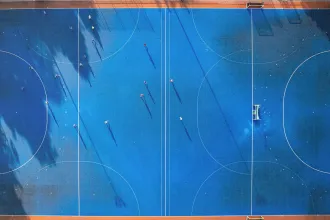 Aerial view of a bright blue sports field with players scattered across the court, casting long shadows in the sunlight