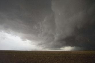 Massive storm cloud spreads dramatically across the sky above a flat, open field