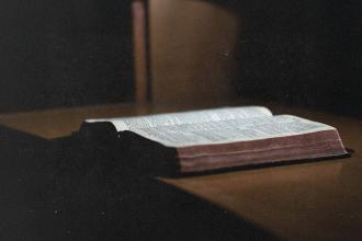 Open Bible resting on a wooden surface in soft, low light