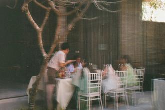 Server attending to a group of people dining at an outdoor restaurant, seen through a glass window with soft motion blur