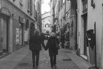 Two people walking hand‑in‑hand down a narrow cobblestone street lined with shops and tall historic buildings
