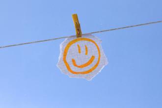 Hand‑drawn smiley face on a torn piece of paper clipped to a clothesline against a clear blue sky