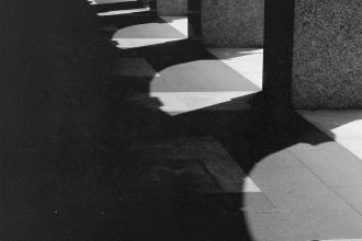 Strong contrast of light and shadow cast by a row of stone columns onto a tiled walkway