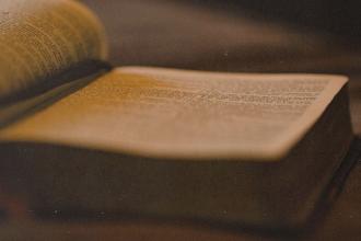 Close-up of an open Bible lying on a table, softly lit with warm, golden light highlighting the printed text