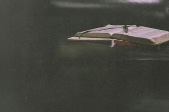 Close-up of an open Bible with a ribbon marker and reading glasses placed on top, set against a dark background