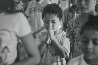 hild standing in a crowded room with hands held together in a prayer posture