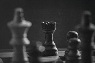 Black-and-white photograph of a chessboard with a wooden rook in sharp focus among blurred pieces