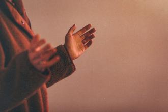 A person extends both hands outward in a gentle, open‑palmed gesture against a warm, softly lit background