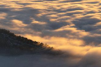 Golden clouds blanket a mountain landscape at sunrise or sunset, with warm light streaming across the ridges