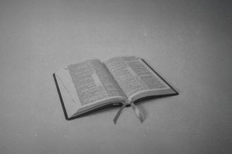 Black‑and‑white image of an open Bible resting on a flat surface with two ribbon bookmarks