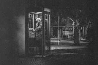 Person standing in a lit phone booth at night on a quiet street
