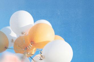 White and golden balloons rising toward a cloudless blue sky