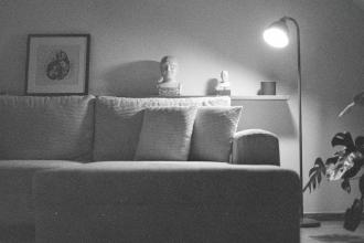 A cozy living room with a soft couch, a floor lamp casting warm light, framed art on the wall, and decorative objects arranged on a shelf