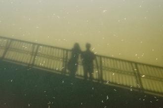 Shadowy silhouettes of two people standing close together on a bridge, captured from below
