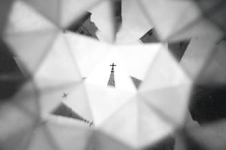 A church steeple topped with a cross is reflected and multiplied through a kaleidoscope‑like pattern of geometric shapes