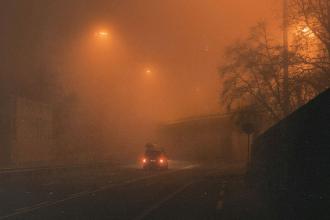 Vehicle driving through dense nighttime fog under glowing overhead lights