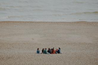 Friends gathered in a circle on a sandy beach near gentle ocean waves